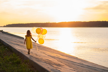 Girl with balloons running on the embankment of the river with the sun at sunset. Graduation in kindergarten