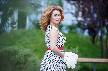 Naklejka premium beautiful red-haired woman in a white dress with black polka dots. Hands with white orchids. Beautiful hair girl. Beauty portrait 