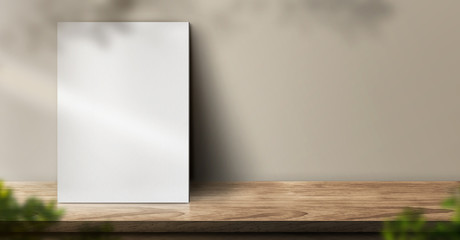 blank poster on wood table background with sunlight window create leaf shadow on wall with blur indoor green plant foreground.panoramic banner mockup for display of product,warm tone lights