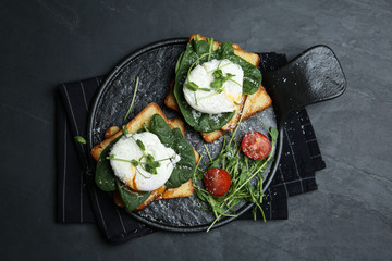 Delicious poached egg sandwiches served on black table, flat lay