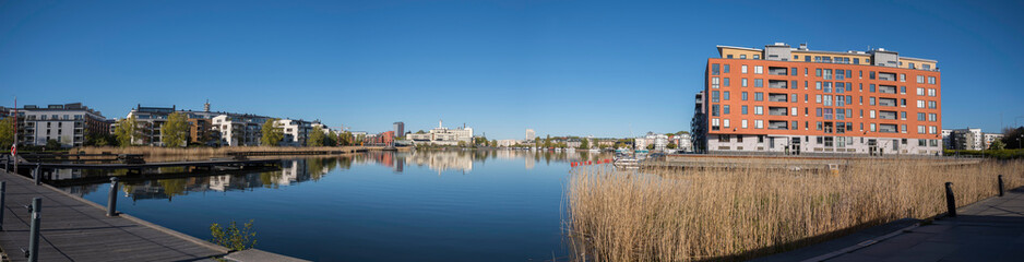 Fototapeta na wymiar View over the bay Hammarby sjö with waterfront buildings and boats at the embarkment a sunny spring morning with water mirror reflecting in Stockholm