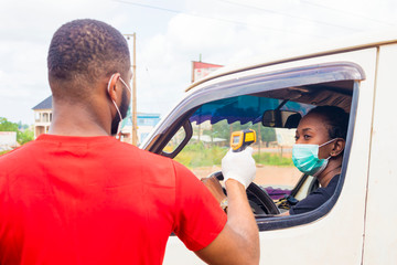 young black man wearing a nose mask, checking the temperature of a black woman driving a car