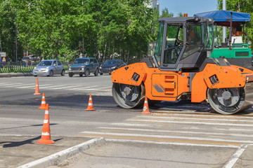 Urban road construction, asphalt paver. A compactor machine for laying new asphalt.
