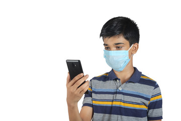 Portrait of Indian young boy using mobile phone and wearing the mask against the coronavirus covid19