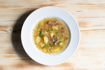 Pea soup with potato, smoked meat, spices in white plate on wooden background