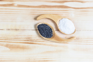 Black (burned with powder) salt and white salt  in  spoons on wooden background