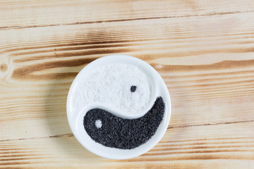 White and black burned mineral salt in Yin Yang bowl on wooden background