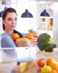 Obraz premium Smiling woman taking a fresh fruit out of the fridge, healthy food concept