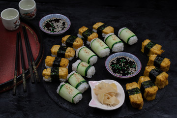 Variety of vegetarian sushi  rice, tamago omelette, cucumber rolls on dark plate alon with pickles and sauce