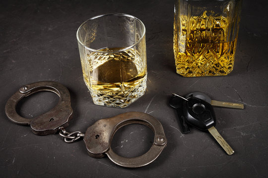 Concept Of Criminal Liability For Driving While Intoxicated. Bakal With Cognac, Handcuffs, Car Key On A Dark Background, Vignetting