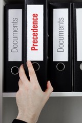 Precedence. Finance/Economics. File Folder is taking by a hand from office shelf. Text is on the...