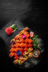 set of sushi roll with salmon, avocado, cream cheese, cucumber, rice, caviar, eel, tuna in plate on black wooden table background