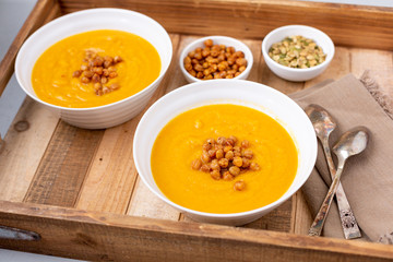 Two Bowls of Homemade Butternut Squash Soup on a Wooden Tray with Garnishes of Roasted Chickpeas and Pumpkin Seeds