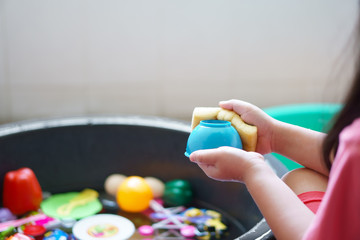 child or kid girl wash and cleaning colorful plastic toy in water basin black by sponge for kill bacteria or dirty disease and dust sterilize from coronavirus covid-19 and closeup hand
