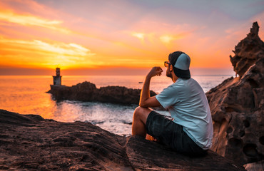 A young man in a white shirt and cap looking at the orange sunset of the Pasajes San Juan...
