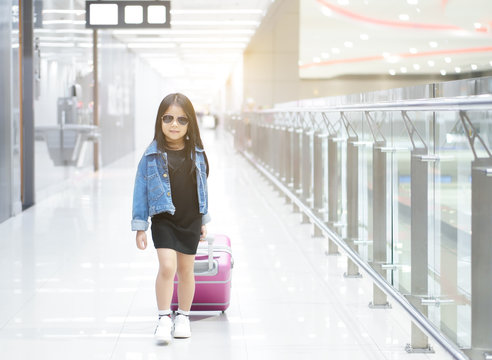 Asian Child Or Kid Girl Walk Dragging Luggage Or Baggage And Pink Suitcase With Wear Sunglasses And Denim Shirt Or Jeans On Walkway In Airport For Holiday Travel Relax And Summer Vacation Trip On Warm