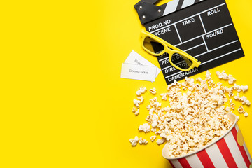 Paper cup with popcorn and movie clapper on a yellow background, place for text