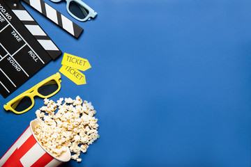 Paper cup with popcorn and movie clapper on a blue background, place for text