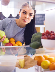 Obraz premium Smiling woman taking a fresh fruit out of the fridge, healthy food concept