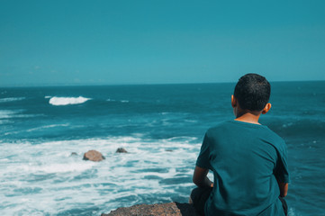 Fototapeta na wymiar A boy sitting on a rock casually looked out at the ocean and the waves