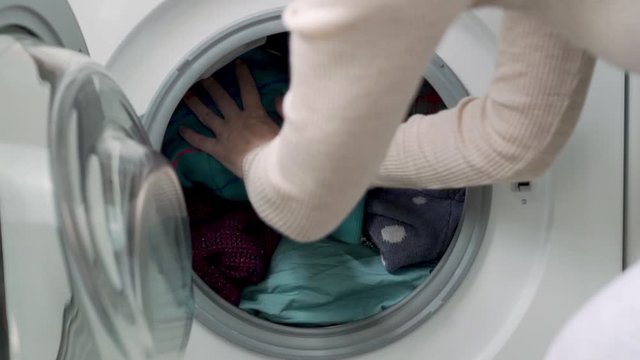 The Girl Puts a Blue Jacket in the Drum of the Washer with Colored Laundry for Washing Close-up. Homework, the process Of preparing for Washing.