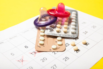Female birth control pills, colored condoms and a calendar. Close-up