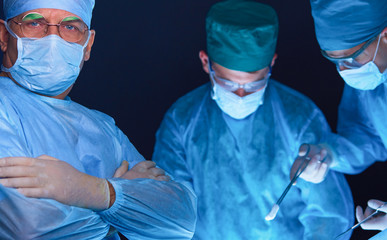 Group of surgeons at work in operating theater toned in blue. Medical team performing operation