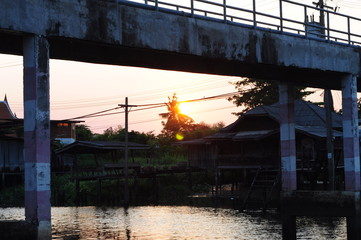 Bridge over the river Old community in Nonthaburi While the sun sets, twilight sky with golden light decorating the horizon while the sun is going to set above the rural area of Thailand .