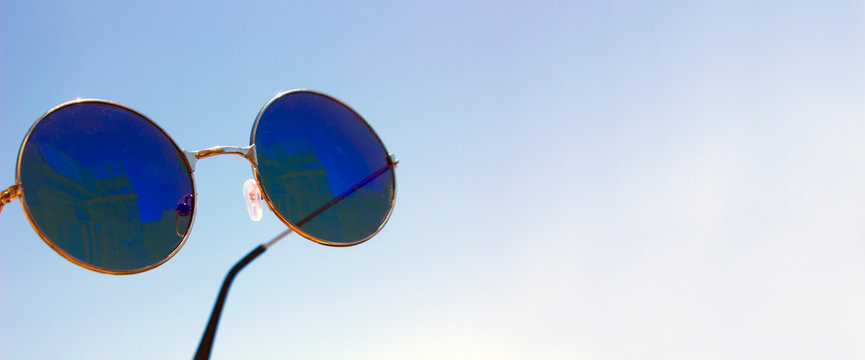 Blue raund vintage Sunglasses against a blue sky, summer accessories. see the future. Space for text. Banner. Mock up. Nobody