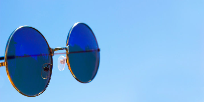 Blue raund vintage Sunglasses against a blue sky, summer accessories. see the future. Space for text. Banner. Mock up. Nobody