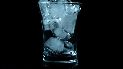 Close-up of melting blue ice cubes in glass with black background