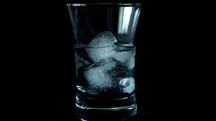 Close-up of melting blue ice cubes in glass with black background