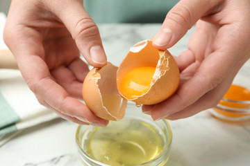 Woman separating egg yolk from white over glass bowl at table, closeup - obrazy, fototapety, plakaty