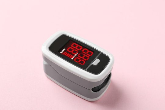 Modern fingertip pulse oximeter on pink background, closeup