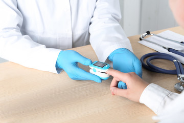 Doctor examining patient with modern fingertip pulse oximeter at wooden table, closeup