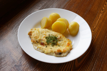 Potato and fish in batter. Appetizer dish in a white plate on a dark wooden background.