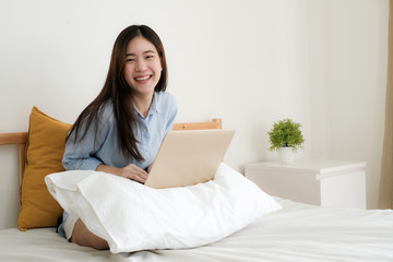 Cute young woman work at home on laptop computer while sitting on bed,looking at camera and brightly smile.