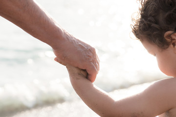 grandparent holding the hand of child at the beach