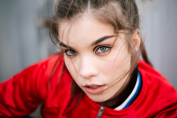 Fototapeta premium Candid portrait of beautiful girl model with creative makeup looking straight at the camera with disheveled brunette hair in red jacket