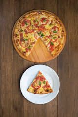 Photograph of Pizza Marguerita made with Mozzarella Cheese, tomatoes, basil leaves and green olives, served on a wooden board.Pizza slice served in a plate aligned with the pizza in the bottom corner.