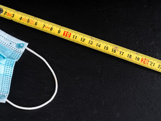 coronavirus icons as facial mask and folding meter on black background representing social...
