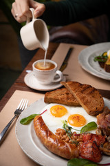 Full English breakfast - fried egg, baked beans, bacon, sausages on a dark rusty background, toasts.