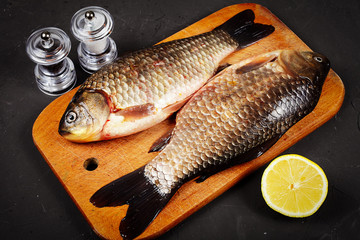 two fresh crucian carp lie on a cutting board, lemon, mills for salt and pepper, vignetting
