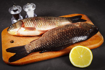 two fresh crucian carp lie on a cutting board, lemon, mills for salt and pepper, vignetting