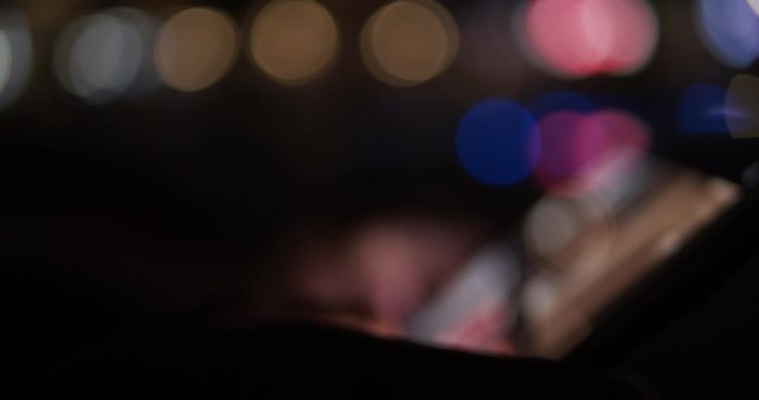 Blurry footage of smart touchscreen device being used at night with bokeh light circles - concept internet business casual lifestyle usage