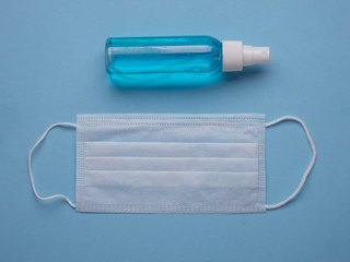 White medical face mask and hand sanitizer on a blue background top view. Coronavirus COVID-19 prevention concept.