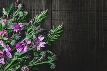Bouquet of wild meadow flowers on dark wooden background. Various spring flowers on wooden table. Top view, copy space for text, close up.