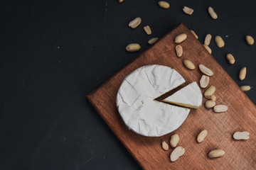 Camembert round cheese and a slice lie on a wooden board. grey matte concrete background. peanut