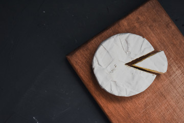 Camembert round cheese and a slice lie on a wooden board. grey matte concrete background.
