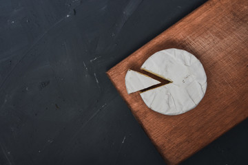 Camembert round cheese and a slice lie on a wooden board. grey matte concrete background.